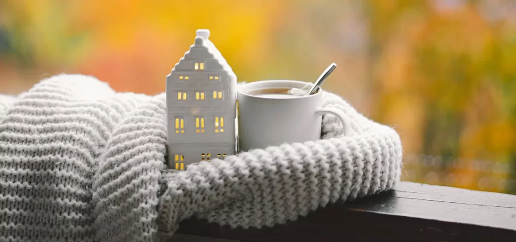 Casita, tacita de café y bufanda blanca del blog de cómo adaptar tu hogar y reducir el consumo energético en invierno