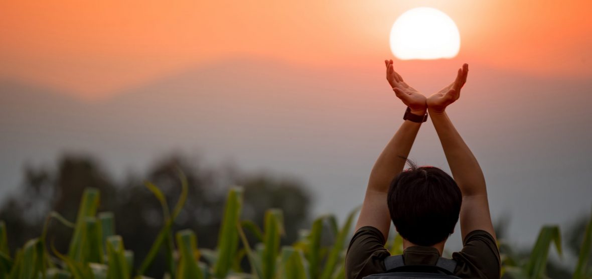 Asian man in corn field raising his arms holding the sun at sunset in summer solstice day. Hope and pray. Achievement concept